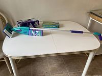 Swiffer Wet Jet mop on a white table along with two boxes of cleaning pads, one opened and one unopened.