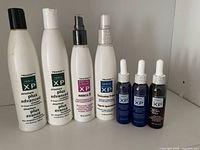 Photo showing seven Triaxon hair care products aligned, including shampoo, conditioner, therapeutic spray, thickening prep, and serums.