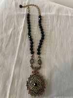 Full view of the locket necklace showing the black faceted bead chain and colorful crystal-encrusted pendant.