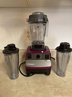 Blender base with 64 oz container, two personal cups, tamper arranged on countertop