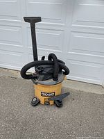 Vacuum upright showing yellow base tank, black hose attached, and flat nozzle on top.