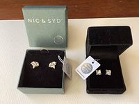 Two sets of Nic & Syd earrings in their original boxes with tags visible, one leaf-shaped and one square-cut Swarovski crystal set.