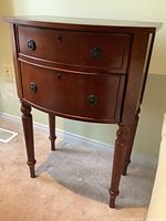 Full front view of the Bombay side table showing curved front, two drawers, four turned legs and reddish-brown finish.