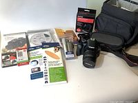 Canon EOS digital camera system with attached lens, instruction manuals, LCD screen protectors, microfiber cloth, and some CD discs on white surface.