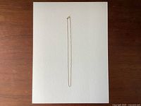 Full photo of delicate yellow gold chain necklace laid flat on textured white background.