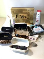 Overview photo showing multiple sunglasses in branded cases, Dove body wash and lotion, and other assorted personal care items.