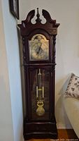 Full view of vintage wooden grandfather clock with arched top and finial, glass door showing pendulum inside.