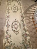 Full length view of the cream colored runner rug with floral and ornamental motifs on carpeted floor near staircase.