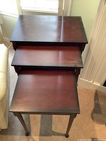 Three wooden nesting tables stacked together showing top surfaces and leg design.