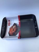 Top view of rectangular, black metal oven roaster pan with paper label showing roasted turkey attached inside shallow pan.