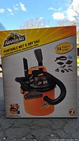 Front view of the box showing the ArmorAll portable wet and dry vacuum in orange and black with 14 included accessories and 2 HP motor detail.