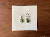 Front view of the pair of silver earrings with bright green settings on white card.