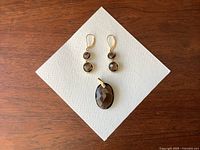 Necklace pendant and earrings displayed on white textured background showing faceted smoky quartz stones set in yellow gold