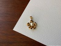 Front angled view of flower-shaped gold pendant with pearl
