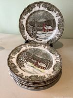 Stack of eight vintage Johnson Bros plates showing snowy village scene with church.