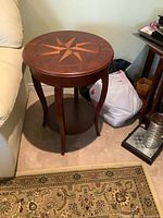 Side view of vintage round wooden side table next to a couch showing four curved legs and lower shelf.