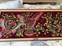 Full view of the framed needlepoint artwork showing two birds with colorful foliage on a deep red background.
