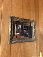 Side perspective photo showing the ornate vintage frame and wall placement of the framed "A Mother's Duty" art print by Johannes Vermeer.