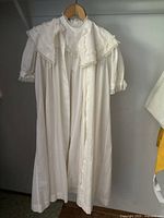 Full view of long white cotton antique Edwardian dressing gown hanging on a hanger showing full length and loose fit.