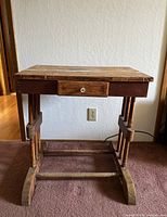 Front view of a wooden trestle small table showing its rectangular top, drawer in the middle, and sturdy trestle legs with curved feet.