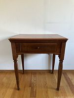 Front view of the antique wooden sewing machine table showing drawer and detailed legs.