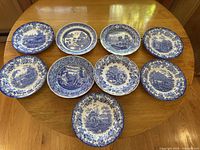 Ten vintage Spode blue and white china plates arranged on a wooden table, showing various scenes and floral borders in detailed blue transferware.
