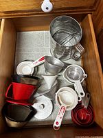 Kitchen drawer with various measuring cups, funnels and a metal sifter inside.