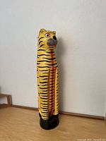Full view of the tall hand-painted wooden cat sculpture with striped pattern on sides and front, showing its size and shape
