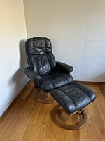 Full view of black leather recliner and matching ottoman on wood floor