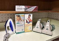 Front angle view of the lot showing all items including boxed heating pads, the iron, cordless vacuums, and massager box on a kitchen counter