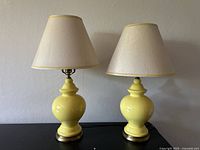 Pair of yellow ceramic mid century table lamps with white fabric shades on a dark surface against a light wall.