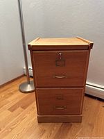 Front view of the 2 drawer wooden file cabinet with key in lock. Shows the file cabinet's overall condition and finish.