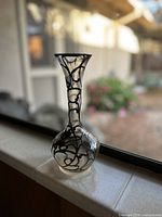 Full view of the vase on a window ledge showing its overall shape and silver overlay design.