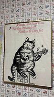 Framed vintage B. Kliban cat poster top angled view on floral wallpapered wall.