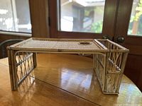 Side view of the vintage bamboo and rattan lap desk placed on a wooden table near glass doors with a garden view.