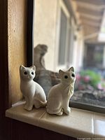 Two small vintage cat figurines placed on a window sill, showing their size and form.