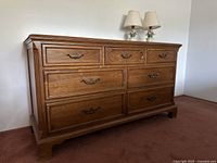 Vintage wooden dresser by Davis Cabinet Company. Nine drawers with metal handles. Located in room with white wall and brown carpet.