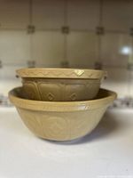 Stacked view of two vintage yellow ceramic mixing bowls showing embossed decorative design.