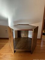 Front view of the hexagonal wooden end table showing brass accents and open shelf