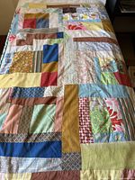 Top view of vintage mid-century patchwork throw quilt blanket laid out flat on a bed, showing the various colored fabric patches arranged in a geometric pattern.