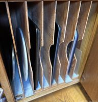 Side view of a wooden cabinet divider holding multiple vintage metal pans including a large rectangular pizza stone