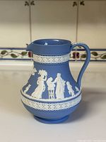 Front view of the Etruscan blue jasperware Wedgwood pitcher with white reliefs depicting classical figures and decorative bands.