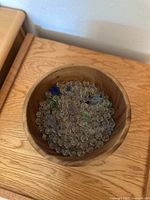 Top-down view of the wooden bowl filled with small clear beads and colored glass marbles in blue and green.