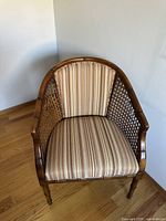 Front angled view of the vintage mid century faux bamboo style accent chair showing striped upholstery and cane sides.