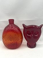 Front view of amberina flask and ruby red owl paperweight side by side on neutral background.