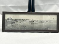 Small framed black-and-white panoramic photograph of Perkins Cove showing harbor village and rocky coastline in Maine, in original wooden frame.