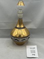 Front view of Art Deco glass decanter with gold finish and black stylized gazelles around midsection, showing the tapered neck and matching glass stopper with gold tip.