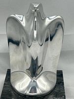 Front view of highly polished abstract Nambe cast metal eagle sculpture on black marble base.