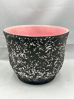 Front view of jardinière showing rounded shape with pink splatter pattern on black exterior and smooth pink interior.