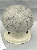 Front-facing photo of vintage frosted glass dome ceiling light with black splatter pattern mounted on white enamel base.